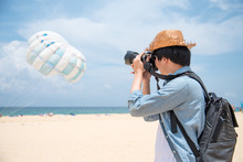 Young Asian Man Photographer In Jean Shirt Take Photo Of Parasailing On The Beach Of Phuket, Thailand