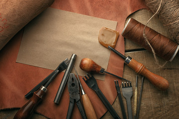 Wall Mural - Set of leather craft tools on wooden background. Workplace for shoemaker. Piece of hide and working handmade tools on a work table.