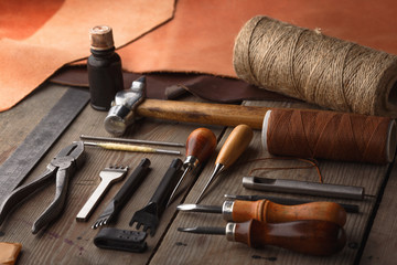 Wall Mural - Set of leather craft tools on wooden background. Workplace for shoemaker. Piece of hide and working handmade tools on a work table.