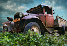 An Old Vintage Rustic Red Colored Truck On A Field With Cloudy Sky Background