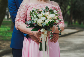 Wall Mural - Wedding couple embrace each other. Groom's hands on bride's waist. Curvy woman in pink lace evening dress. Wedding bouquet with white, beige roses and eustoma with eucalyptus. Plus size bride.