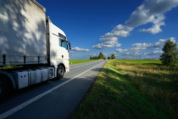 White truck driving on the asphalt road in the countryside on a sunny day with blue sky and white clouds