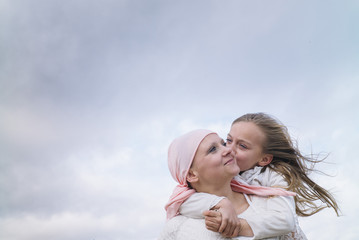 a woman with cancer is next to her daughter. a girl is hugging a woman happy