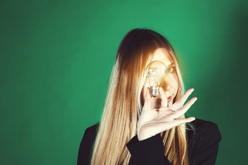 Wall Mural - Serious pretty business woman holding a light bulb on a green background. Model looks through the glass on the bulbs. Concept of a green world for the future of our children