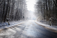 Icy Country Road Leads Through A Winter Forest With Bare Trees And Snow, Concept For Safety Transport And Traffic In The Cold Season