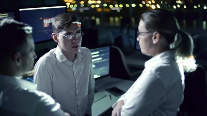 Team of IT professional programmers discussing plans in cyber security center filled with display screens