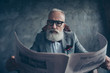© deagreez - Attractive, smart, cool, old businessman in glasses and jacket reading newspaper, news about politic, bitcoin, finance, economy, science over gray background, sitting in chair