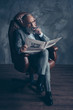 © deagreez - Full length portrait of brutal old man in tux holding, reading, looking at newspaper, smoking cigar, sitting in armchair, leg on leg, shares, money, stock, gray background