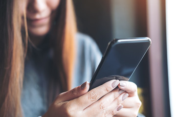 Closeup image of a beautiful Asian woman holding , using and looking at smart phone in modern cafe