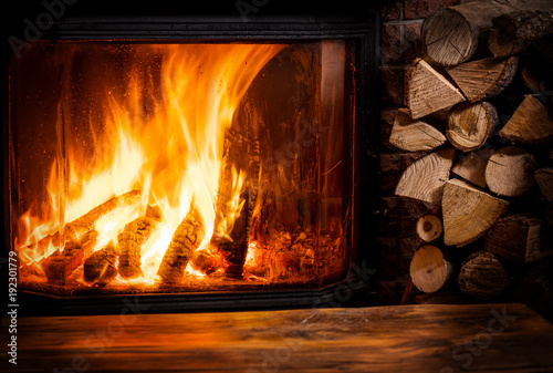 Fotomural Old wooden table and fireplace with warm fire at the background.