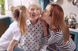 Love our granny. Cute little girl and her mother kissing a senior woman on the cheeks together while the woman smiling happily