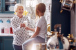 © zinkevych - Be healthy. Charming caring elderly woman giving a glass of milk to her little granddaughter and smiling at her while the girl sitting on the kitchen counter