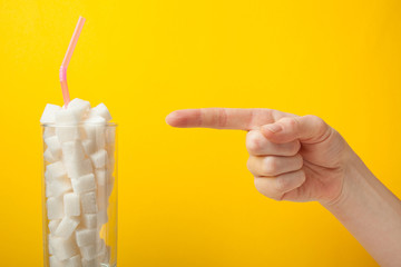 The hand points to the glass with sugar on a yellow background.