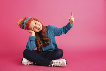 Wall Mural - Cheerful redhead girl pointing up at copy space isolated