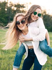 Wall Mural - Two young women are having fun on the field. One girl is riding on another.