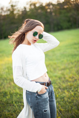 Wall Mural - Young woman with sunglasses is posing on the green field.