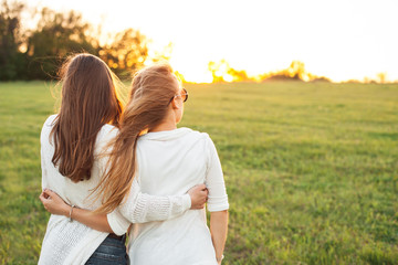 Wall Mural - Two young women are looking forward tothe sunset on the green field.