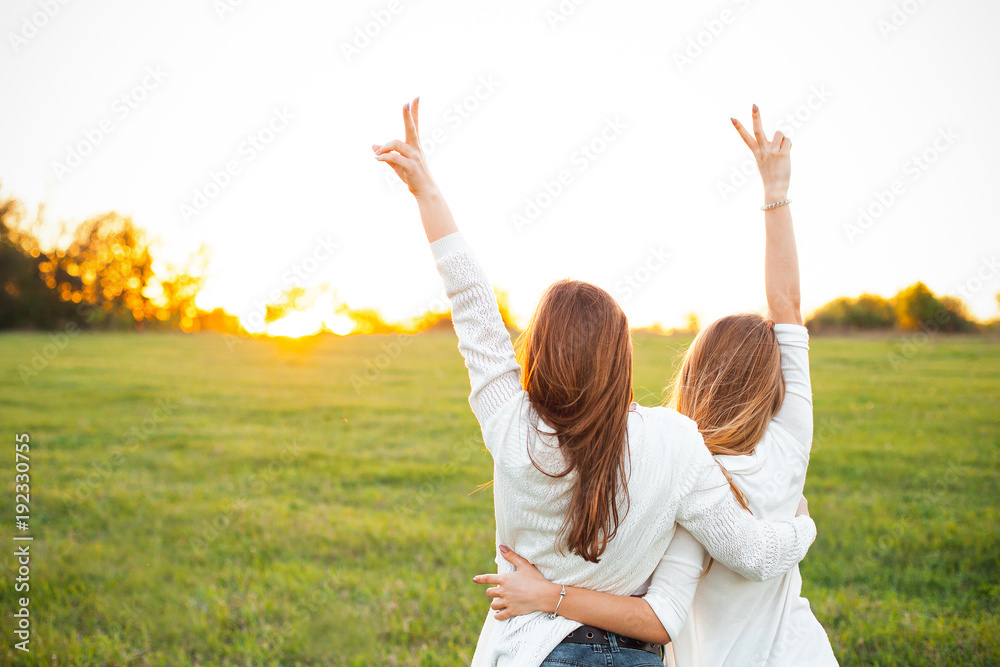 Two women in white sweaters are looking on the sunset. Best friends - obrazy, fototapety, plakaty 