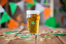 Glass Of Beer, Shamrock And Coins On Wooden Table
