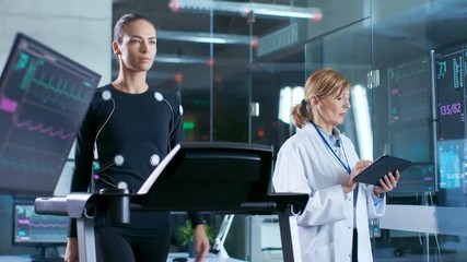 Wall Mural - woman athlete walks on a treadmill with electrodes attached to her body while scientist holding tabl