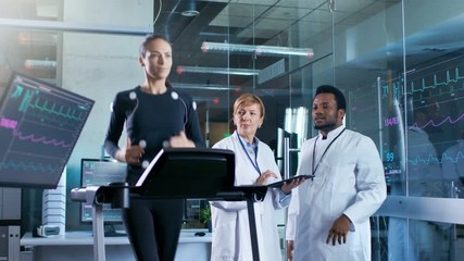 Wall Mural - woman athlete runs on a treadmill with electrodes attached to her body while two scientists supervis