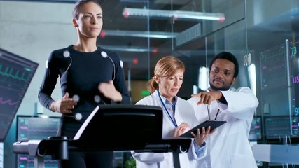 Wall Mural - woman athlete runs on a treadmill with electrodes attached to her body while two scientists supervis