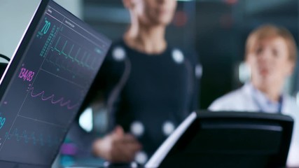 Wall Mural - monitor showing ekg reading of a woman athlete running on a treadmill in the background, two special