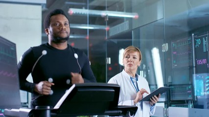 Wall Mural - male athlete runs on a treadmill with electrodes attached to his body while sport scientist supervis