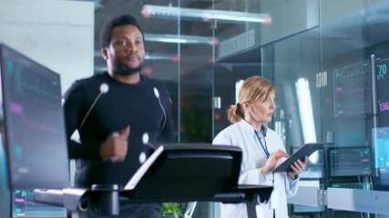 Wall Mural - male athlete runs on a treadmill with electrodes attached to his body while sport scientist holds ta