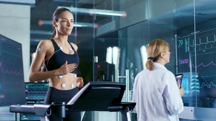 Wall Mural - beautiful woman athlete runs on a treadmill with electrodes attached to her body, female physician i