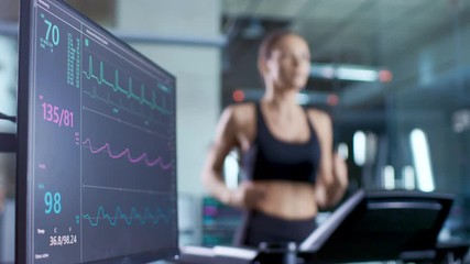 Wall Mural - medical monitor shows ekg reading of a woman athlete running on a treadmill. focus on monitor.