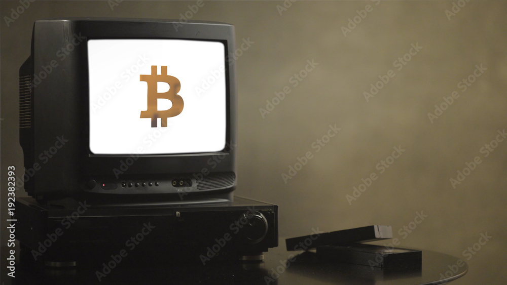 Vintage television on wood table with bitcoin. Old TV showing bitcoin. Near the TV there are film cassettes and video player