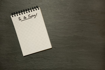 To do list on gridded spiral notepad on grey slate table top - from above, minimalism 