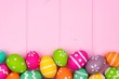 Colorful Easter egg bottom border against a pink wood background. Top view with copy space.