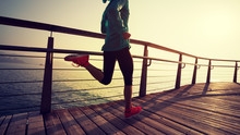 Sporty Fitness Female Runner Running On Seaside Boardwalk During Sunrise