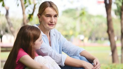 Wall Mural - Mother and daughter relaxing on grass in a park. Family and lifestyle concept