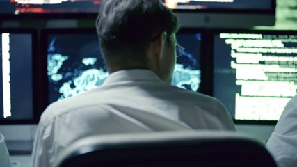rear view of professional team of it security specialists talking in front of multi-display workstat