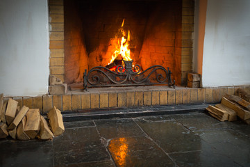 A roaring fire within a large stone arched fireplace, with pile of logs.