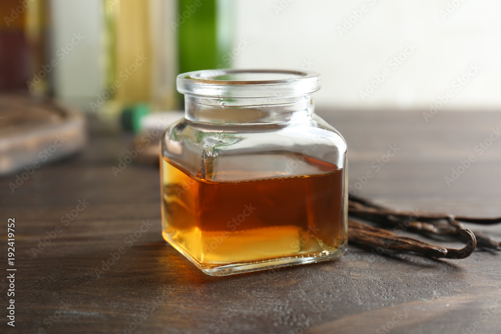 Jar with vanilla extract and sticks on wooden table