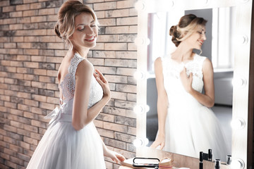 Wall Mural - Beautiful young bride in white wedding dress with makeup created by professional artist near mirror indoors