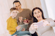 © zinkevych - Love my boys. Upbeat young woman taking a selfie of herself and her husband and son while they having breakfast and watching something on tablet