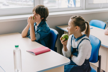 classmates sitting at desk and eating apples on break