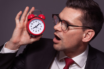 Portrait of handsome businessman wearing glasses and formal attire with an amazed face and holding clock