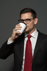 Wall Mural - Portrait of handsome businessman wearing glasses and formal attire drinking coffee on gray background.