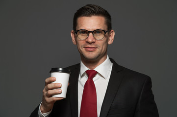 Wall Mural - Successful businessman with glasses and formal suit posing with coffee mug on gray background