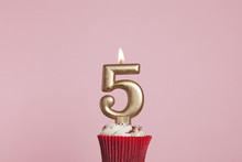 Number 5 Gold Candle In A Cupcake Against A Pastel Pink Background