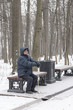 © YuSafa - Man - elderly pensioner, sits on a park bench in the winter. High trees, a lantern.