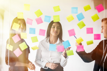 Wall Mural - Three businesspeople discussing and planning concept. Front of glass wall marker and stickers. Startup office.