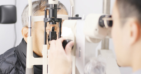 Old man checking on eye in clinic