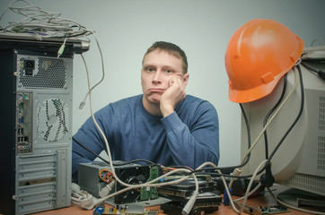 Wall Mural - Tired and bored computer repairman is sitting on his workplace and thinking. Computer technician tired from his work and users.